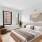Bedroom with bed, end tables, a green plant, dresser, mirror and two windows.