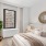 Bedroom with bed, mirror, green plant, end tables, and one window with curtains.